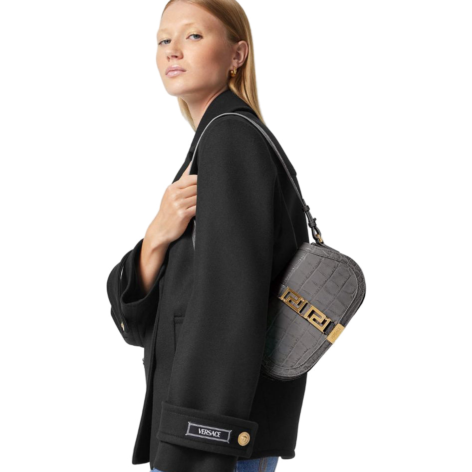 Person holding a black jacket with a gray bag featuring gold accents on a white background