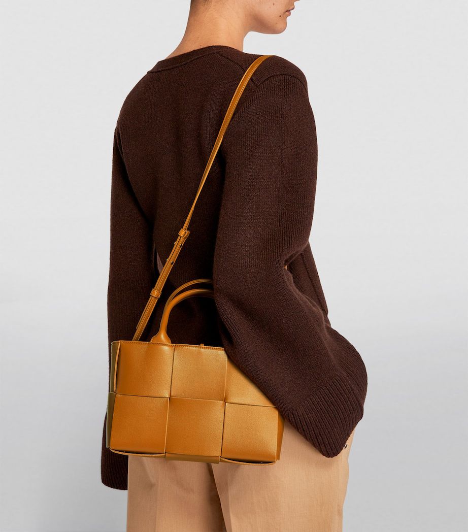 Person wearing a brown sweater with a woven brown handbag on a light gray background