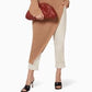 Woman wearing a brown ribbed sweater and white pants, holding a red clutch.