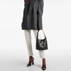 Person wearing a gray pinstripe blazer and white pants, holding a black handbag on a white background
