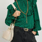 Person wearing a green blouse with ruffles, holding a cream handbag with a gold chain.
