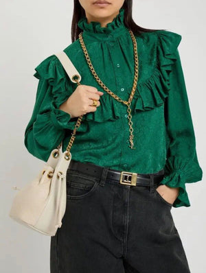 Person wearing a green blouse with ruffles, holding a cream handbag with a gold chain.