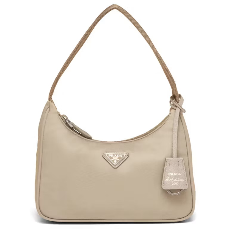 A beige Prada shoulder bag with a curved top, a single shoulder strap, a zippered top closure, and a hanging leather tag on a white background.