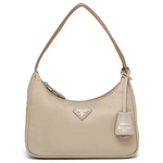 A beige Prada shoulder bag with a curved top, a single shoulder strap, a zippered top closure, and a hanging leather tag on a white background.