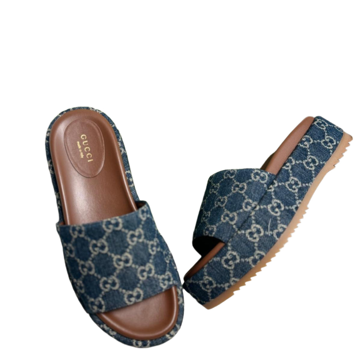 A pair of blue denim Gucci slide sandals with a platform sole and mid-heel, placed on a couch next to a green Gucci box.