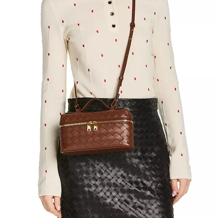 Woman wearing a white blouse with red polka dots and a brown quilted handbag.