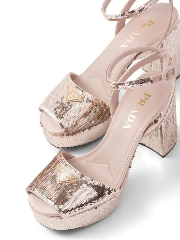 Pair of gold high-heeled Prada shoes with glittery platform and decorative elements on a white background