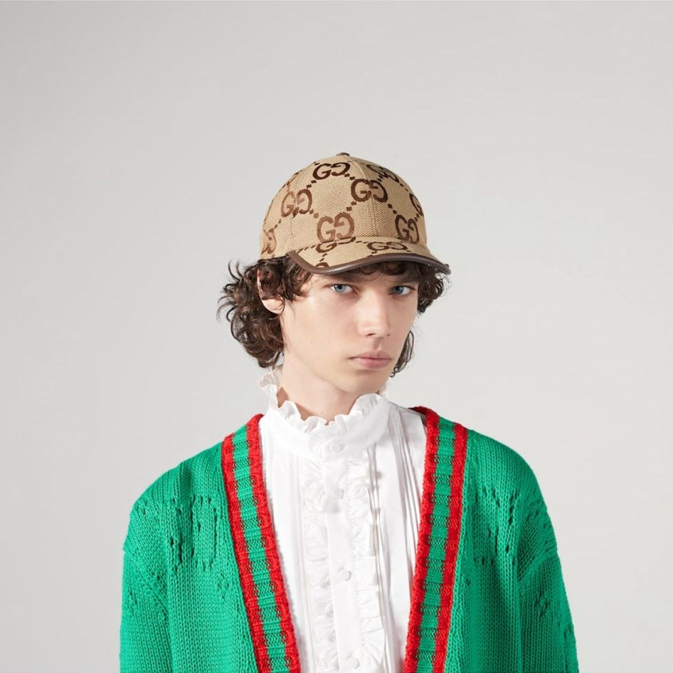 Person wearing a Gucci cap and green cardigan with red and white stripes on a plain background