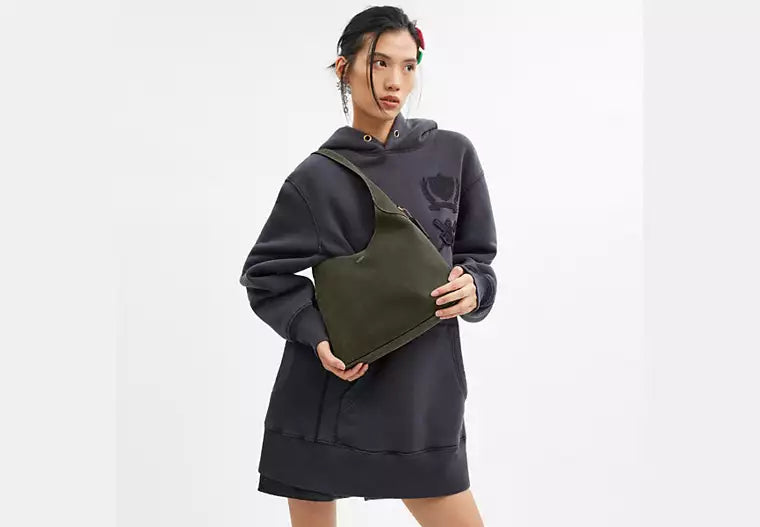 Person wearing a black and gray hoodie with a green pouch on a white background