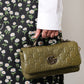 Green Gucci handbag held by a person wearing a floral dress.